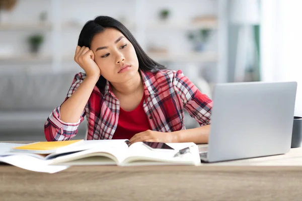 Annoiato giovani asiatico femmina studente seduta a scrivania con computer portatile a casa — Foto Stock