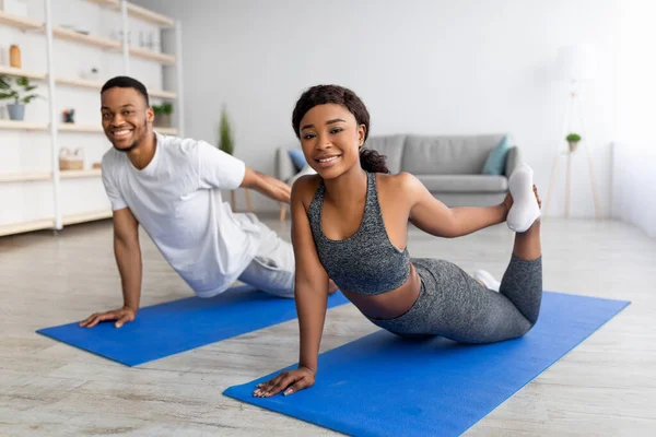 Ejercicios de flexibilidad para una vida saludable. Ajuste pareja negra estirando sus piernas durante el entrenamiento en casa — Foto de Stock