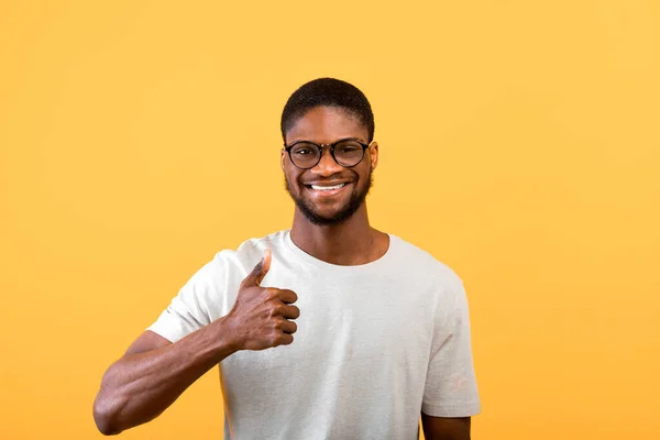 Eu gosto disso. Joyful homem negro gesticulando polegar para cima, aprovando e recomendando algo sobre fundo amarelo, estúdio tiro — Fotografia de Stock