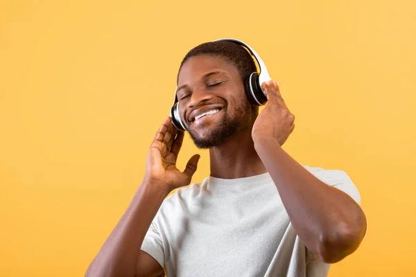 Tiempo libre con música favorita. Feliz chico afroamericano en auriculares escuchando lista de reproducción en el fondo amarillo — Foto de Stock