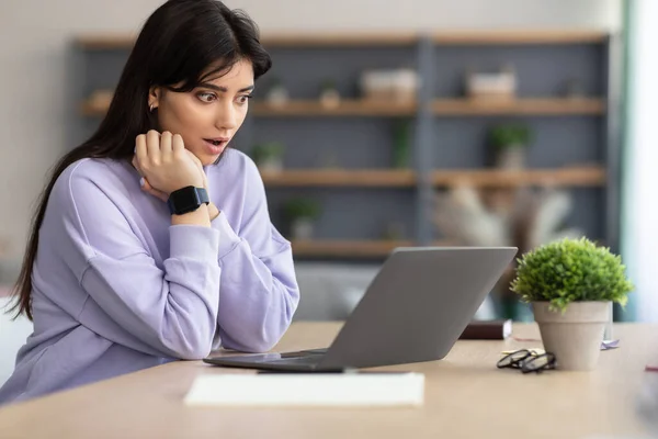 Verrast aziatische vrouw zitten op de bank, met behulp van laptop — Stockfoto