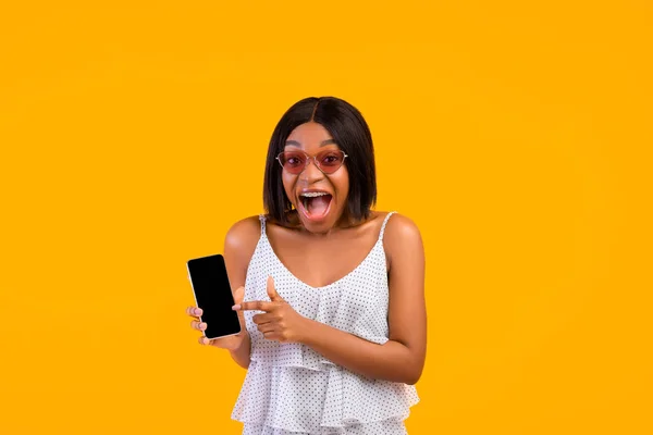 Online καλοκαιρινές εκπτώσεις. Μαύρη κυρία με δροσερό ντύσιμο άνοιγμα στόμα σε κατάσταση σοκ, δείχνοντας στο smartphone με λευκή οθόνη, mockup — Φωτογραφία Αρχείου