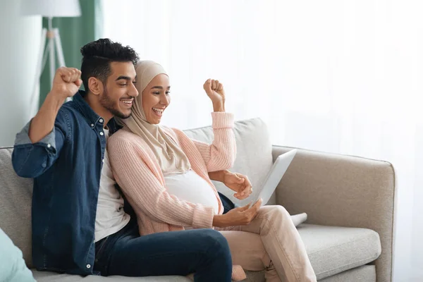 Entusiasmado casal muçulmano grávida comemorando o sucesso com tablet digital em casa — Fotografia de Stock