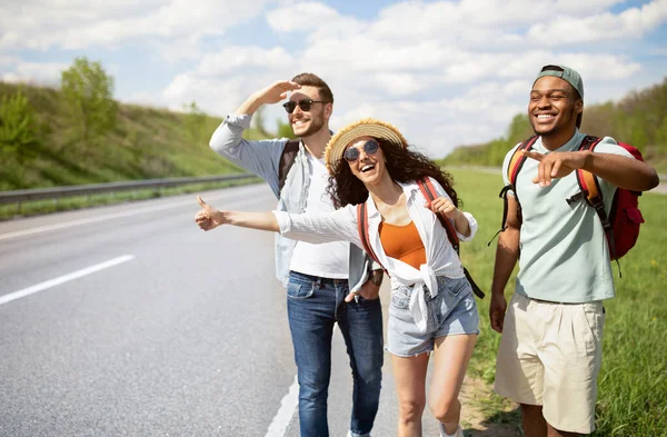 Diversos amigos de pé na beira da estrada, parando carros, carona para passeio grátis, desfrutando de férias de verão — Fotografia de Stock