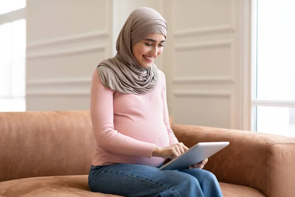 Вид сбоку беременной мусульманки с помощью планшета дома — стоковое фото