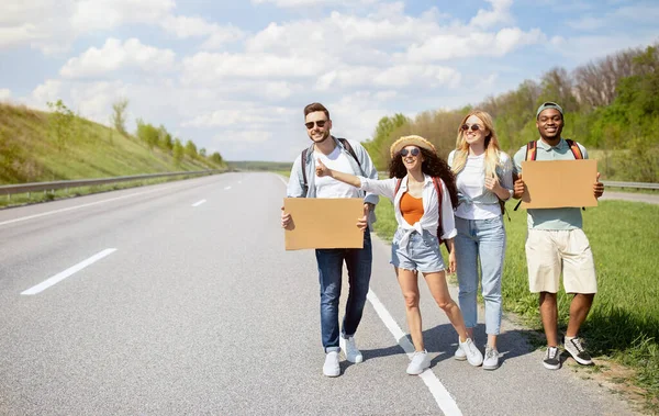 Grupo de amigos multiétnicos com sinais vazios carona na estrada, pegar passeio, viajar por autostop, espaço de cópia — Fotografia de Stock