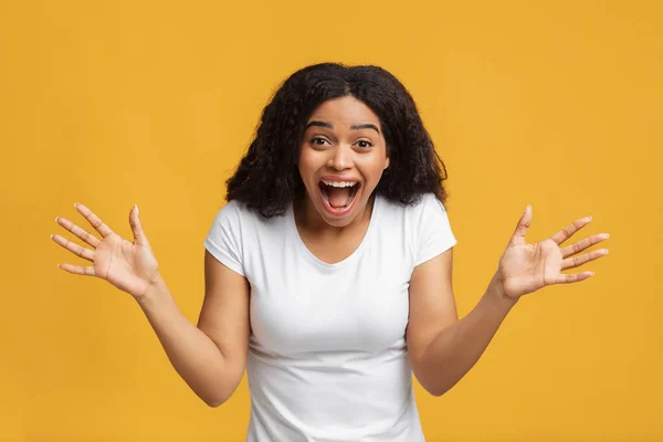 Unglaublich. Überglückliche afrikanisch-amerikanische Frau breitet vor gelbem Hintergrund ihre Hände aus und drückt ihre Überraschung aus — Stockfoto