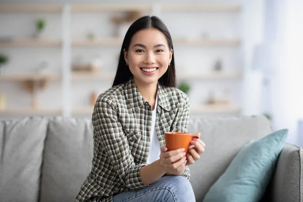 Vrolijke Aziatische dame die koffie drinkt in de woonkamer — Stockfoto