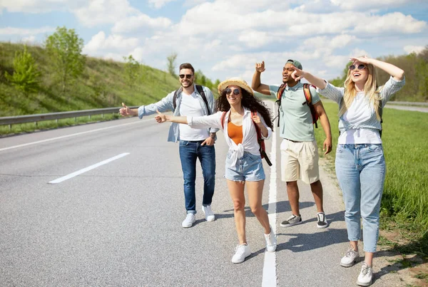 Grupo de jovens em pé na beira da estrada, parando de carro com gestos de carona, divertindo-se viagem de carro, espaço de cópia — Fotografia de Stock