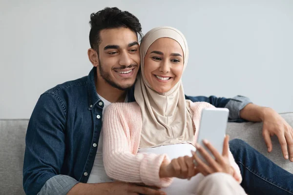 Vidám terhes közel-keleti házastársak Böngészés Internet Smartphone együtt otthon — Stock Fotó