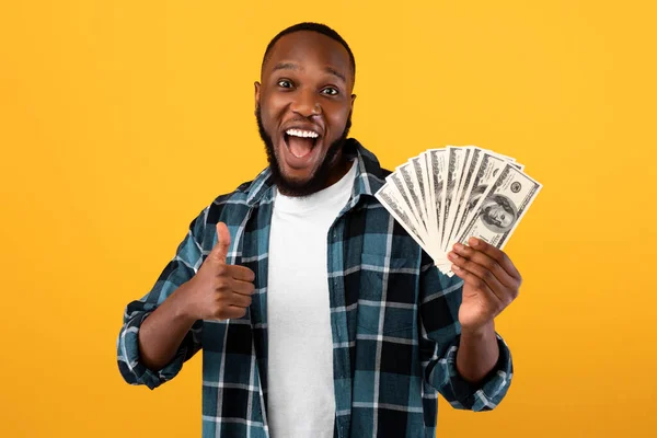 Feliz rico negro chico celebración dinero gestos pulgares arriba, fondo amarillo — Foto de Stock