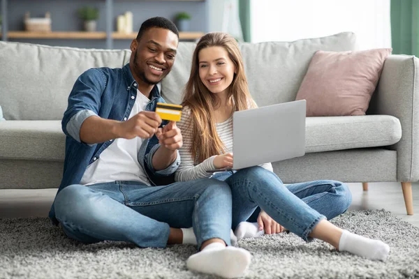 Paiements en ligne. Jeune couple interracial avec ordinateur portable et carte de crédit à la maison — Photo