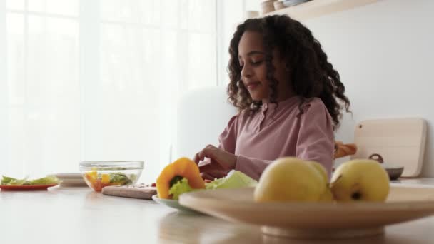 Söt lockigt liten afrikansk amerikansk flicka matlagning hälsosamt mellanmål, äta skivad tomat i köket, slow motion — Stockvideo