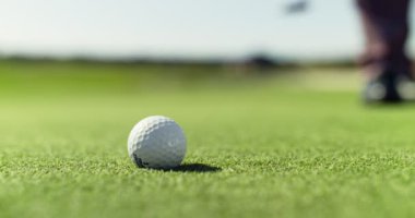 Tanımlanamayan bir adam golf topunun bulunduğu yeri belirliyor. Yeşil çimlerin üzerinde topa geliyor. Yaklaş.