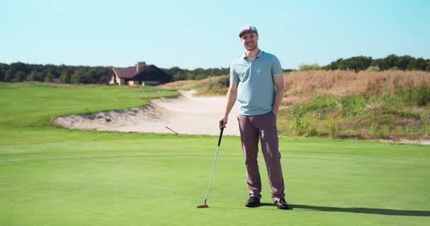 Pasatiempo deportivo de lujo. Al aire libre de hombre feliz jugador de golf posando con el club de golf en el prado verde y sonriendo a la cámara — Vídeos de Stock