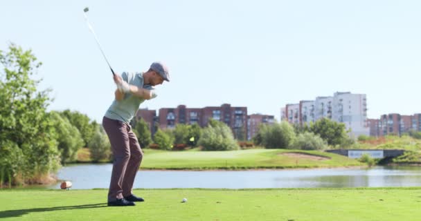 Young male player driving golf on green grass of professional golf course, swinging and hitting golf ball at lake — Stock Video