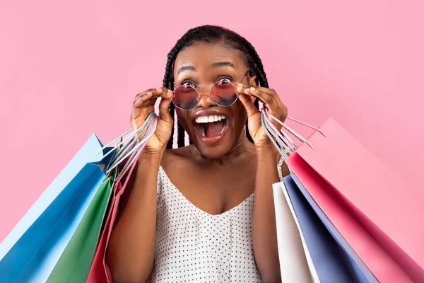 クールな黒の女性でアフロバンチを保持ショッピングバッグ、サングラスに触れると、大きな販売、ピンクの背景を信じることができない — ストック写真
