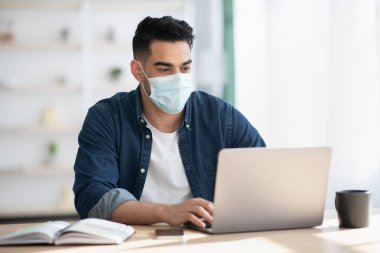 Laptop kullanan koruyucu maskeli bir Arap.