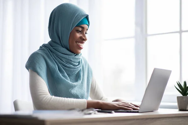 Trabalho remoto. feliz preto muçulmano freelancer senhora no lenço de cabeça usando computador portátil — Fotografia de Stock
