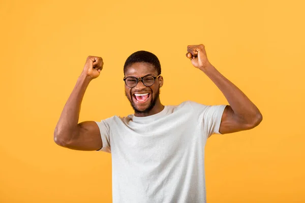 Emocional homem afro-americano gritando WOW em emoção, levantando os braços acima de sua cabeça sobre fundo amarelo — Fotografia de Stock