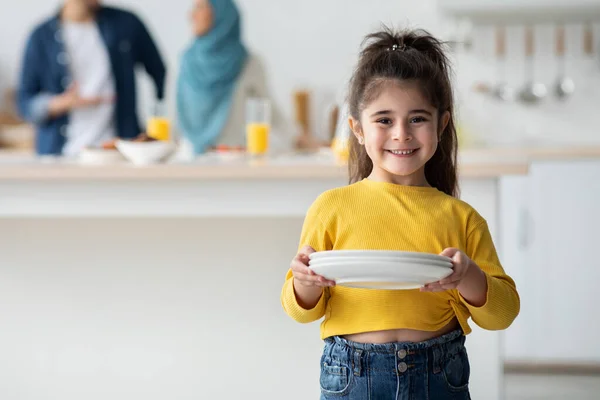 Ayudante. Linda chica árabe sosteniendo placas en la cocina, sonriendo a la cámara — Foto de Stock