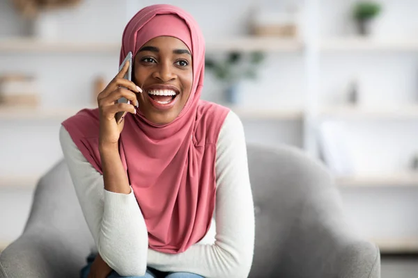 Wesoły czarny islamski kobieta w Hijab rozmawia przez telefon komórkowy w domu — Zdjęcie stockowe