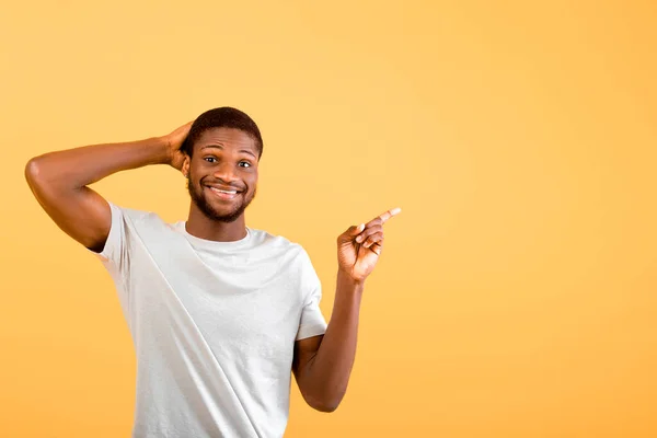 Jovem afro-americano cara apontando dedo de lado anunciando seu texto no fundo do estúdio amarelo, — Fotografia de Stock