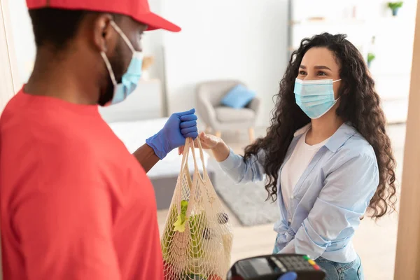 Black deliveryman in medical mask giving net bag to woman — Stock Photo, Image