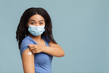 Antiviral bağışıklık. Siyah kadın covid-19 'a karşı aşılanmış, kolunda alçı var, mavi arka planda duruyor.