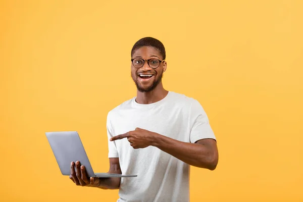 Zaskoczony czarny mężczyzna wskazujący na ekran laptopa z otwartymi ustami, stojący z pc na żółtym tle studio — Zdjęcie stockowe
