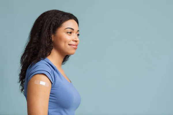 疫苗接种后的概念。Covid-19注射后，快乐的黑人女士，手臂上贴上胶布，蓝色背景 — 图库照片