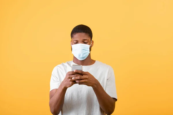 Self-isolation and social media during COVID-19 epidemic. Black man in protective mask using smartphone