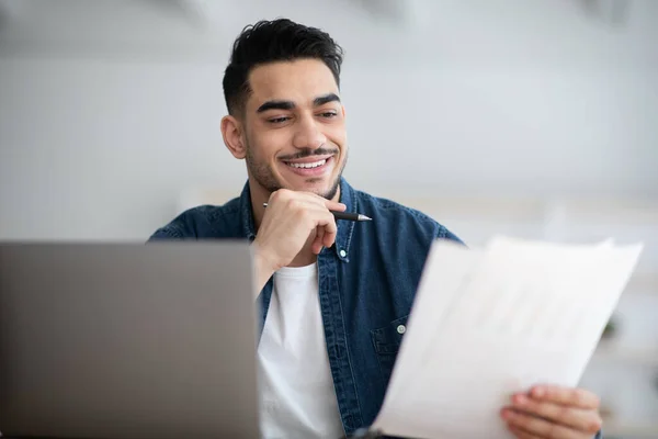 Lächelnder arabischer Geschäftsmann, der im Büro arbeitet, Laptop benutzt, Dokumente liest — Stockfoto