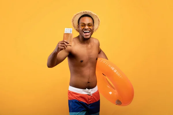 Chico negro feliz sosteniendo el anillo inflable, pasaporte y boletos, yendo al extranjero al país caliente, pasando vacaciones en la playa —  Fotos de Stock