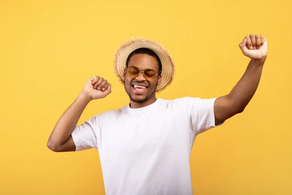 Clubs de verano. Joven negro bailando con su música favorita con las manos en alto sobre fondo amarillo —  Fotos de Stock