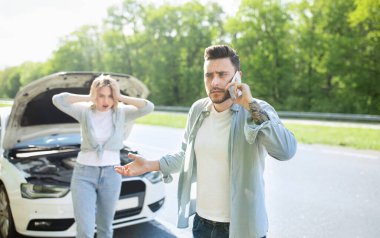 Delikanlı, korkmuş kız arkadaşıyla birlikte bozuk arabanın yanında duruyor. Araba kazası geçiriyor, tamirhaneyi arıyor.