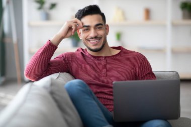 Kanepede dizüstü bilgisayarı olan pozitif Arap adam.