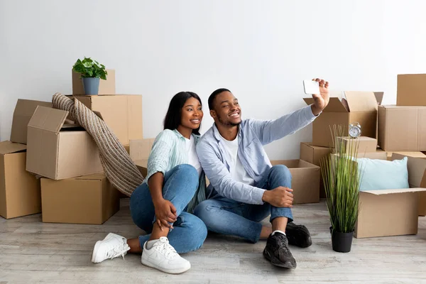 Feliz casal negro se mudar para sua própria casa e tirar selfie entre caixas de papelão, espaço livre — Fotografia de Stock