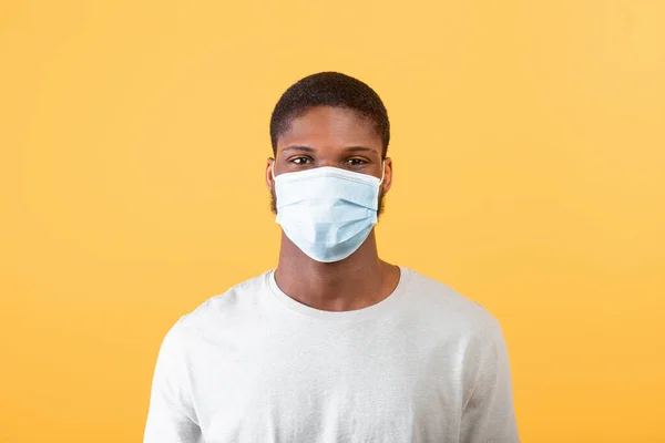 Porträtt av svart kille i medicinsk ansiktsmask tittar på kameran på gul bakgrund, studio skott — Stockfoto