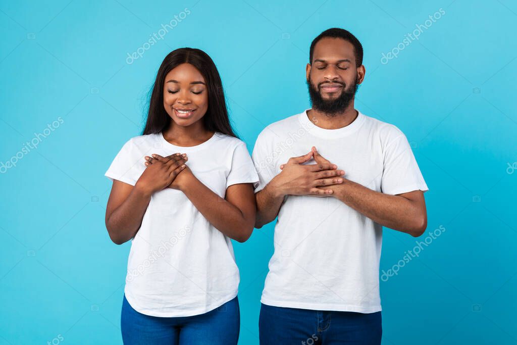 Black couple keeping hands on chest at studio