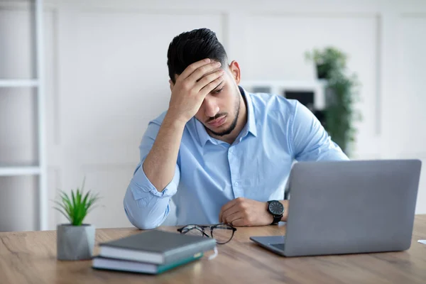 Hombre de negocios árabe milenario cansado que sufre de dolor de cabeza en el escritorio en la oficina moderna — Foto de Stock