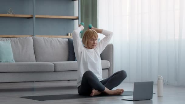 Esportivo mais velha mulher se exercitando no laptop levantando halteres em casa — Vídeo de Stock