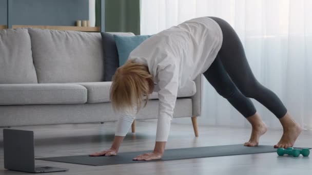 Starsza pani robi jogi rozciąganie mając lekcje online w domu — Wideo stockowe
