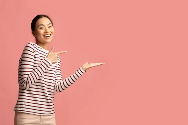 Sehen Sie sich das an. Positive junge Asiatin zeigt auf ihre offene Handfläche — Stockfoto