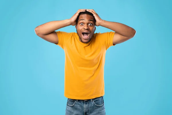 Geschokt Afro-Amerikaanse man schreeuwen aanraken hoofd over blauwe achtergrond — Stockfoto