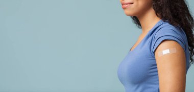 Aşı hayat kurtarır. Aşılanmış kolunda alçı, mavi arka plan, boş alan panoraması olan siyah bir kadın.