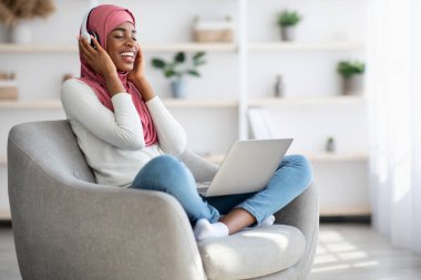 Kablosuz kulaklıklı mutlu zenci kadın evde müzik dinliyor.