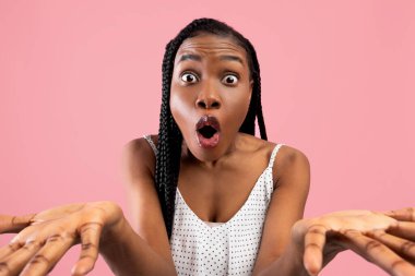 Arican Amerikalı kadın kameraya bakıp pembe stüdyo arka planında el kol hareketi yaptı.