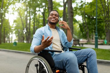 Yeşil Park 'ta tekerlekli sandalyedeki neşeli engelli adam akıllı telefondan konuşuyor.