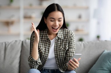 Duygusal Asyalı kadın evde akıllı telefon kullanıyor.